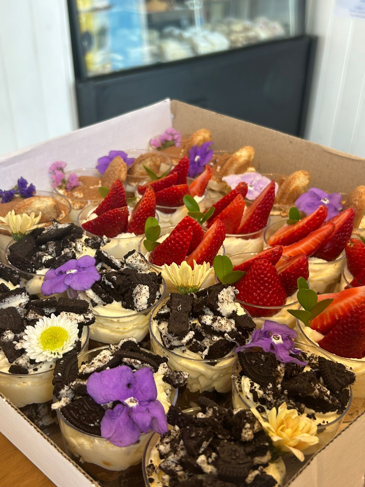 Vasitos de postres con frutillas, Oreo y flores comestibles de una mesa dulce de Antojitos